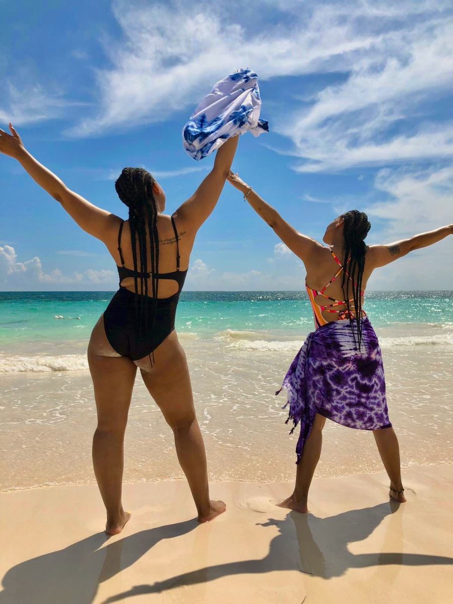 2 women standing on the beach with arms outstretched to the sky