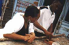 Chris watches Omar Junior, a wood carver, at work.